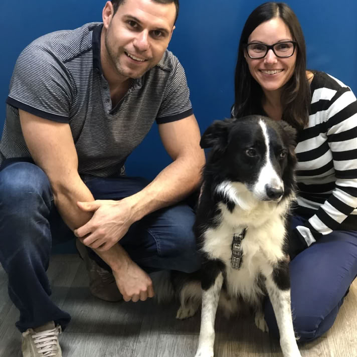 Chico y chica con un perro border collie negro y blanco agachados en la clínica veterinaria El Jardín.